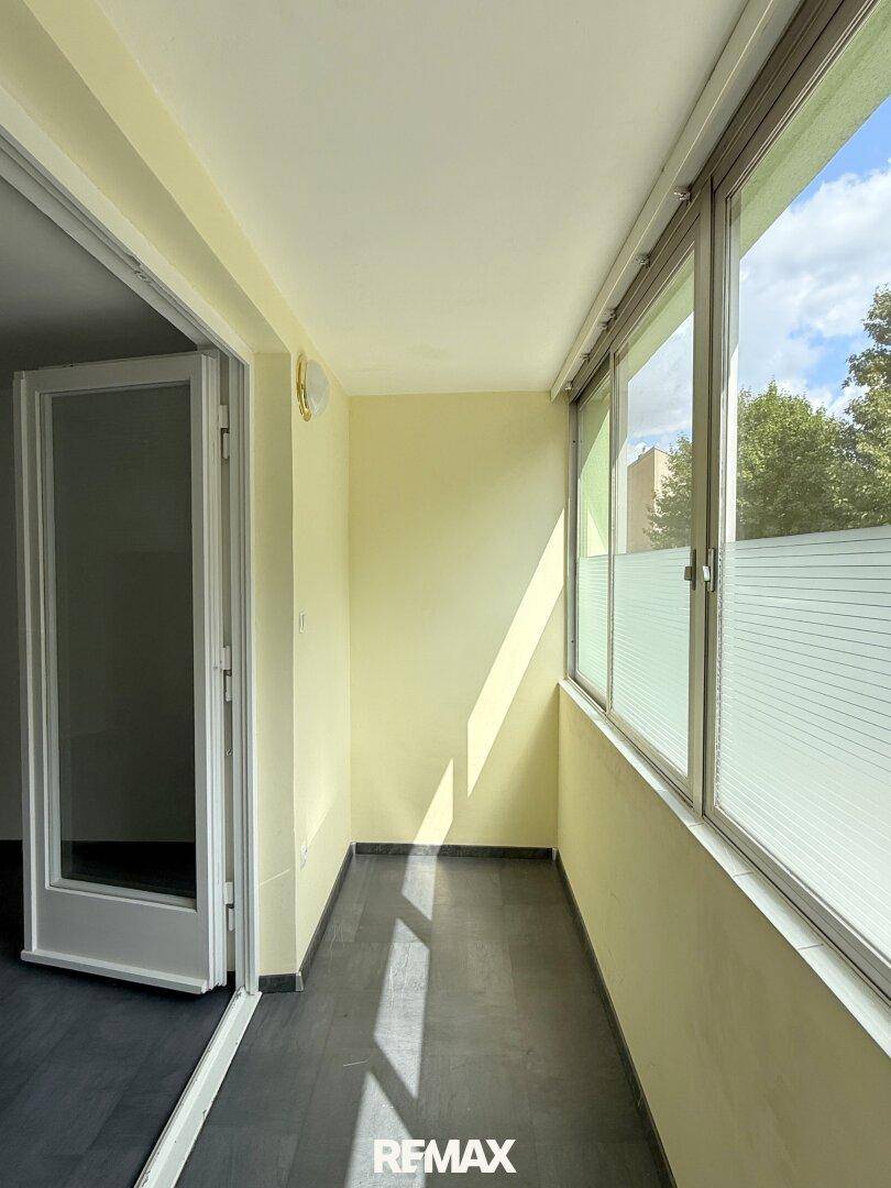 Verglaste Loggia mit hellem Anstrich und Blick ins Grüne, bietet zusätzlichen geschützten Wohnraum.