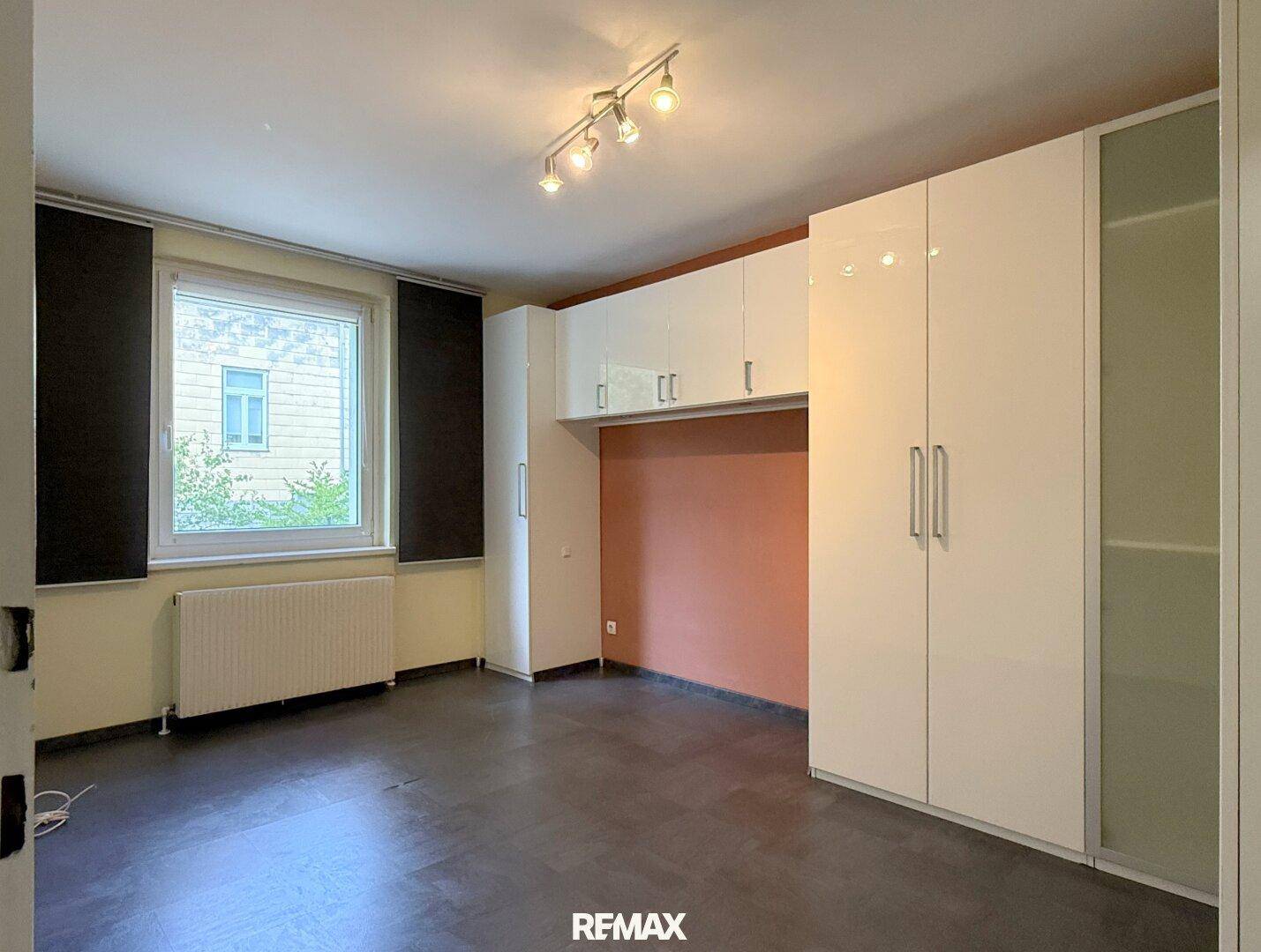 Schlafzimmer mit integrierten Einbauschränken, dunklem Boden und Fenster für natürliche Belichtung.