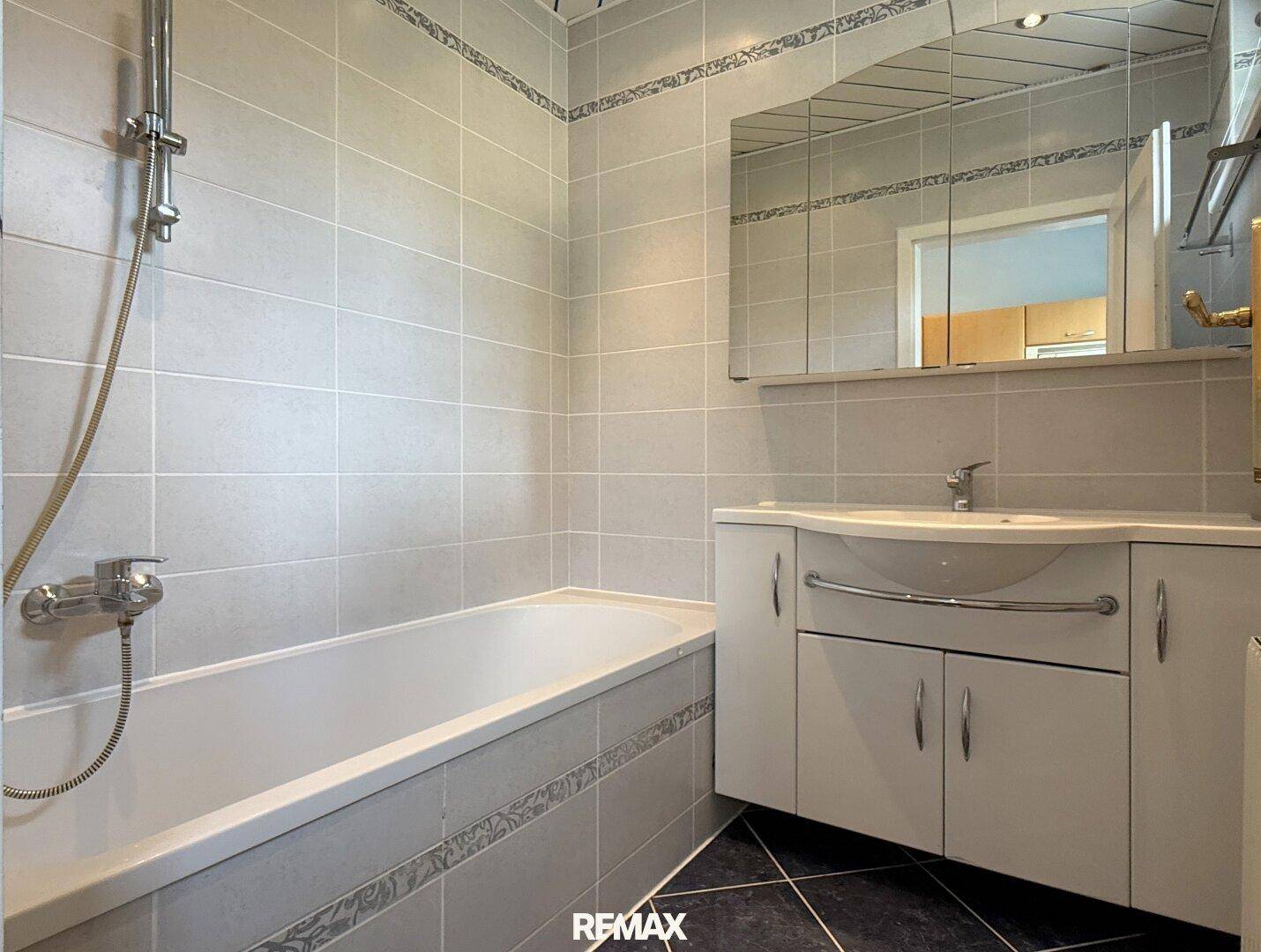 Gefliestes Badezimmer mit Badewanne, Waschtisch und Spiegelschrank, in gutem und modernem Zustand.
