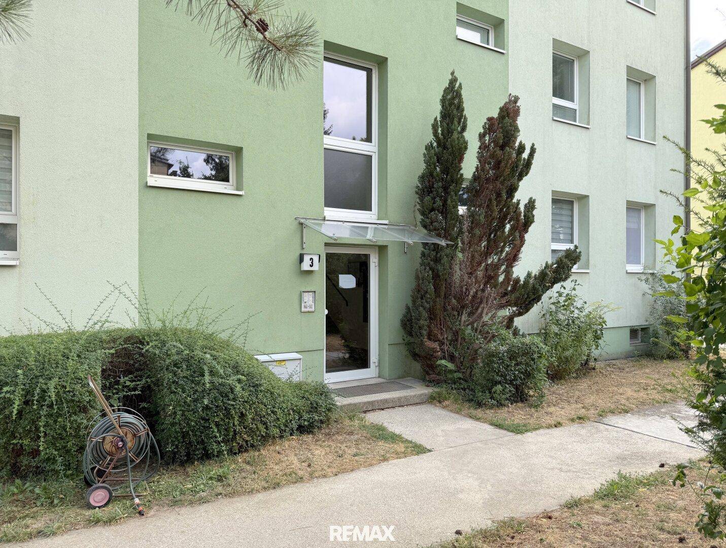 Eingangsbereich eines Mehrfamilienhauses mit grüner Fassade und gepflegter Bepflanzung.