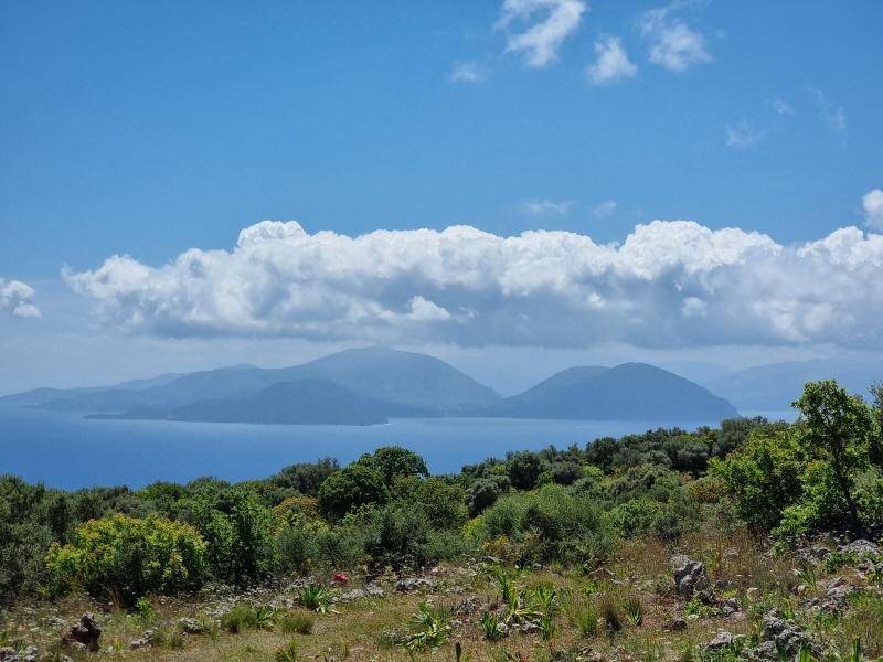 Panoramablick auf das Meer mit fernen Bergen und üppiger Vegetation unter bewölktem Himmel.