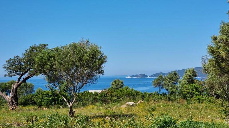 Panoramablick über grüne Hügel und das azurblaue Meer mit kleinen Inseln am Horizont.