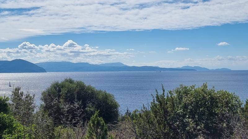 Breiter Blick über das ruhige Meer und die ferne Küstenlinie mit bewaldeten Hügeln unter einem weiten Himmel.