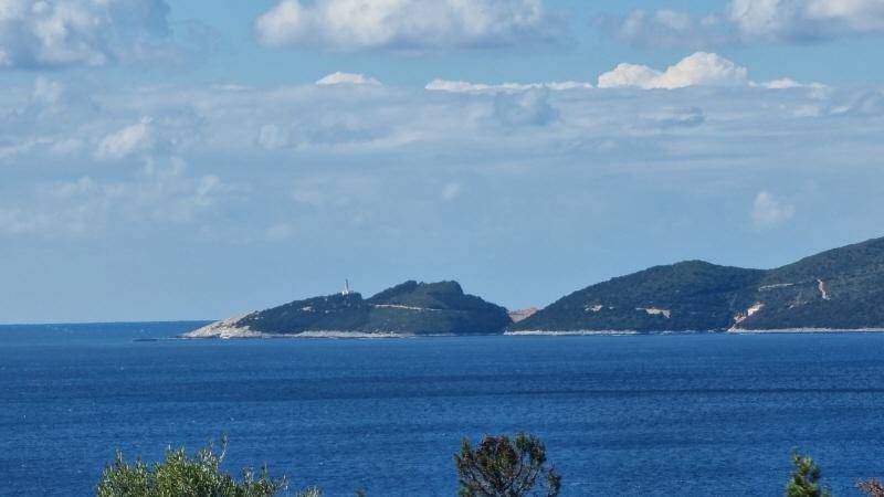 Klarer Blick auf die weite See und die hügelige Küstenlandschaft mit einem Leuchtturm in der Ferne.