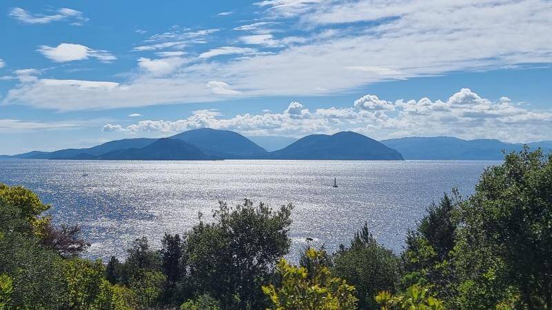 Sonniger Blick auf das weite, glitzernde Meer mit einem Segelboot und den majestätischen Bergen im Hintergrund.