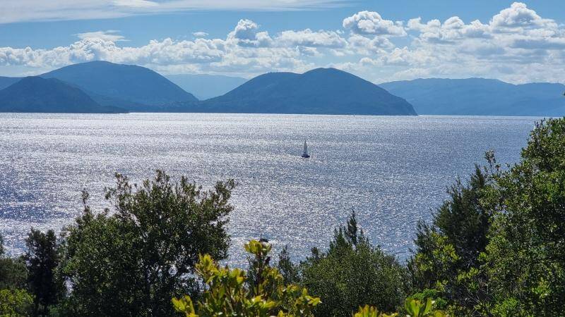 Atemberaubender Ausblick auf das weite Meer mit einem Segelboot und majestätischen Bergen am Horizont.