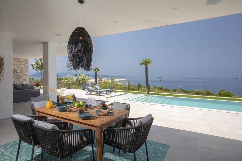 Überdachter Essbereich im Freien mit Holztisch, Blick auf den Pool und das glitzernde Meer.