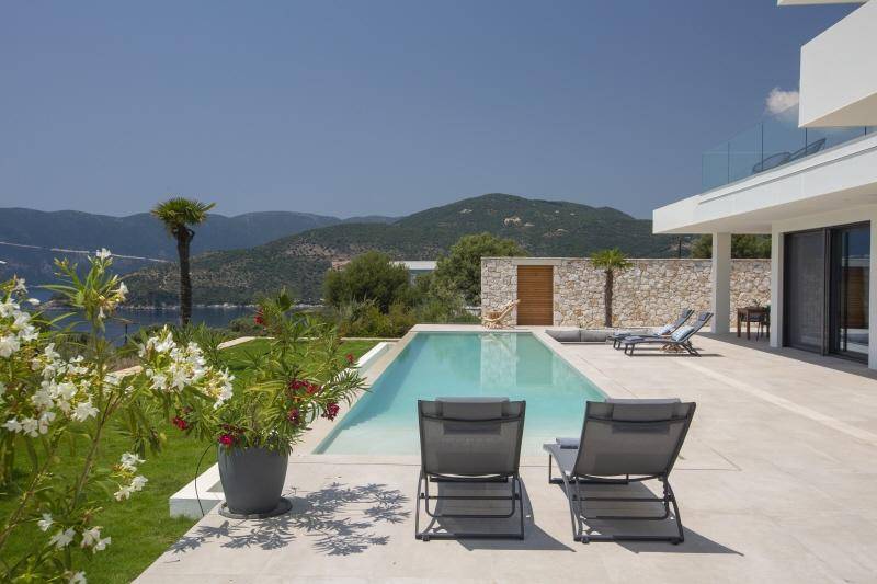 Entspannender Poolbereich mit Liegestühlen, blühendem Garten und malerischem Blick auf Meer und Berge.