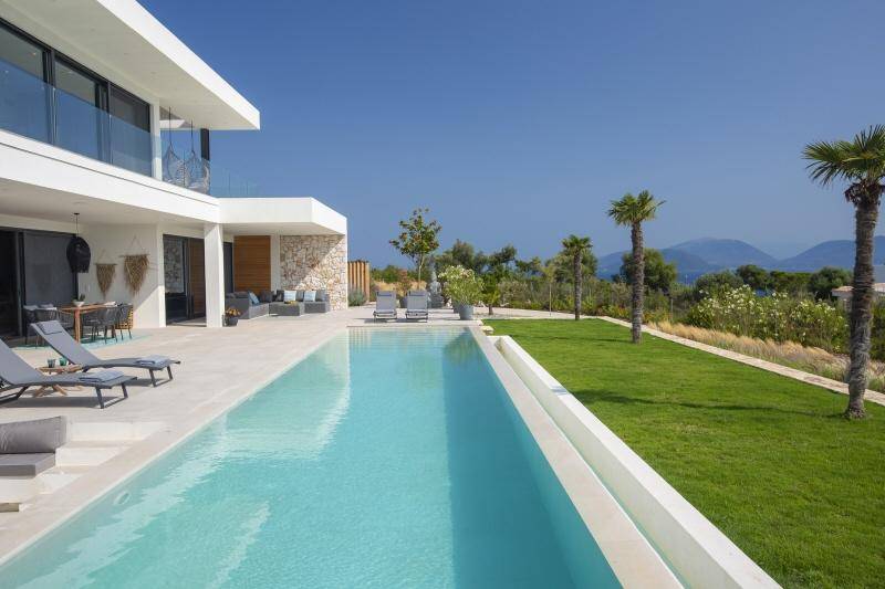 Langer Pool mit Rasenfläche, Palmen und weitem Blick auf das Meer und die umliegende Landschaft.