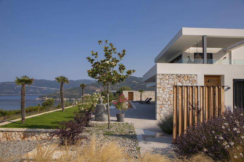 Gepflegter Gartenbereich mit mediterranen Pflanzen, Steinmauer und Blick auf das Meer und die Berge.