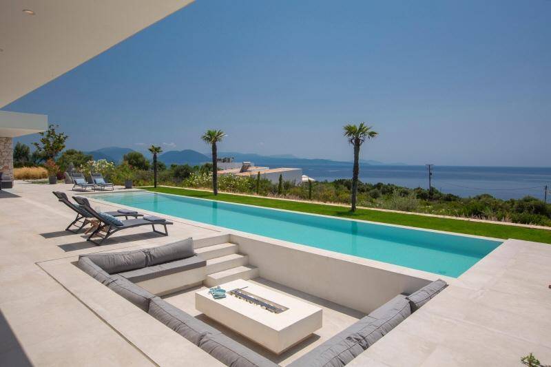 Langer Poolbereich mit versunkener Lounge, Feuerstelle und atemberaubendem Blick auf das Meer und die Berge.