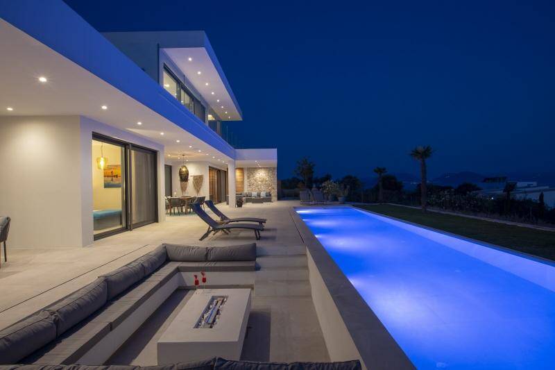 Elegante Villa bei Nacht mit blau beleuchtetem Pool und stilvoller versunkener Lounge mit Feuerstelle.