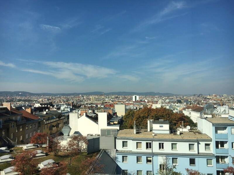 Weitläufiger Panoramablick über eine dicht bebaute Stadtlandschaft mit vielen Dächern und einem klaren blauen Himmel.