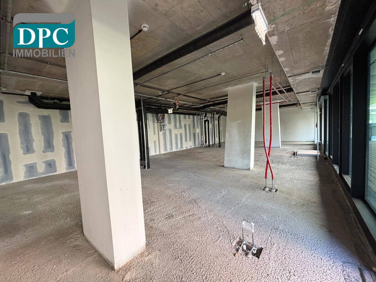 Geräumiger, unfertiger Bürobereich mit Betonoberflächen und großen Fenstern, bereit für den Innenausbau.
