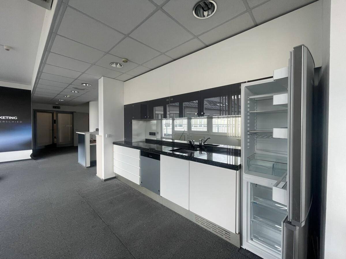 Moderne Küchenzeile mit weißen und grauen Schränken, Spüle und integrierten Geräten in einem Bürobereich.