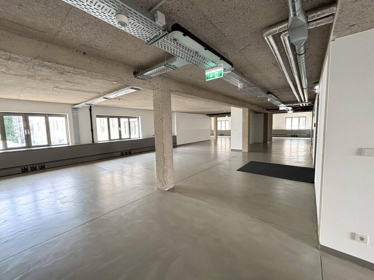 Großer, offener Büroraum mit Sichtbetondecke, Industriedesign und vielen Fenstern für natürliches Licht.