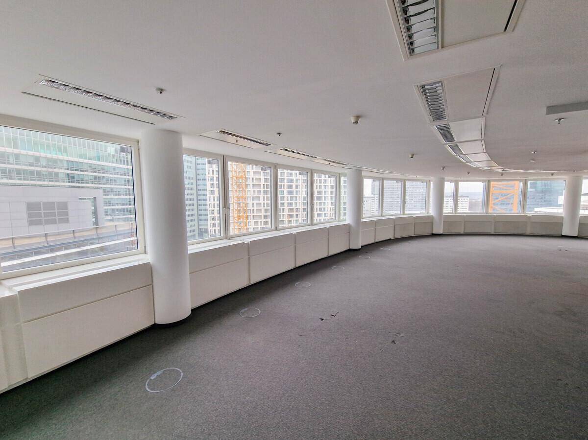 Großzügiges, leeres Büro mit Teppichboden und einer langen Fensterfront, die viel Tageslicht bietet.