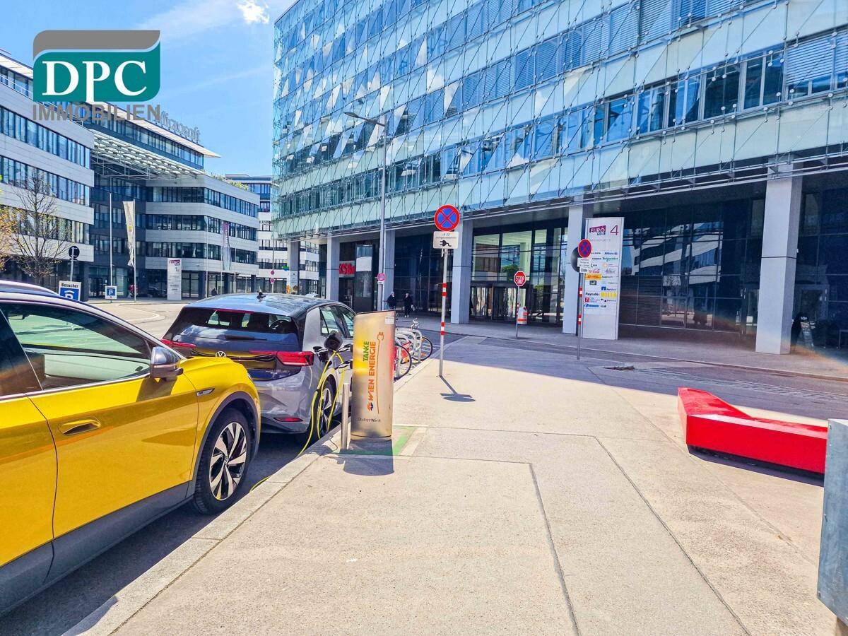 Modernes Bürogebäude mit Glasfassade und Ladestationen für Elektrofahrzeuge auf dem Bürgersteig.