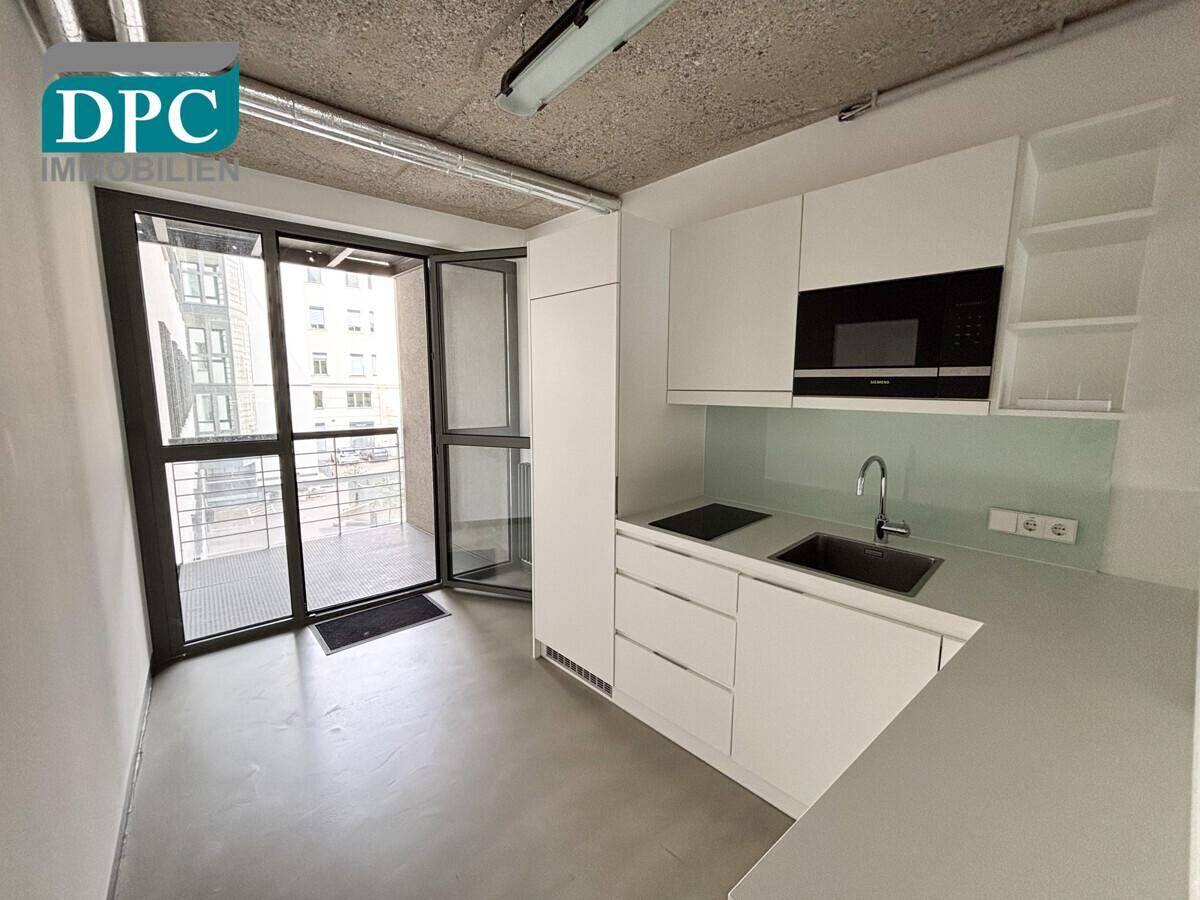 Moderne Teeküche mit weißen Schränken, Einbaugeräten und direktem Zugang zu einem Balkon.