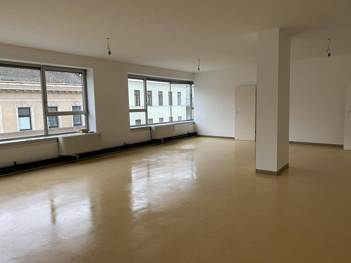 Heller, leerer Büroraum mit großen Fenstern und glänzendem Boden, ideal für flexible Arbeitsplatzgestaltung.