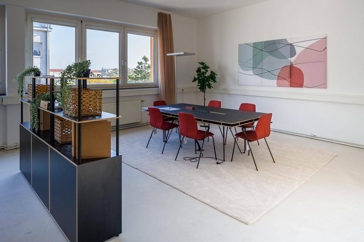Konferenzbereich mit großem Tisch, roten Stühlen, einem Teppich und Blick auf die Umgebung durch die Fenster.