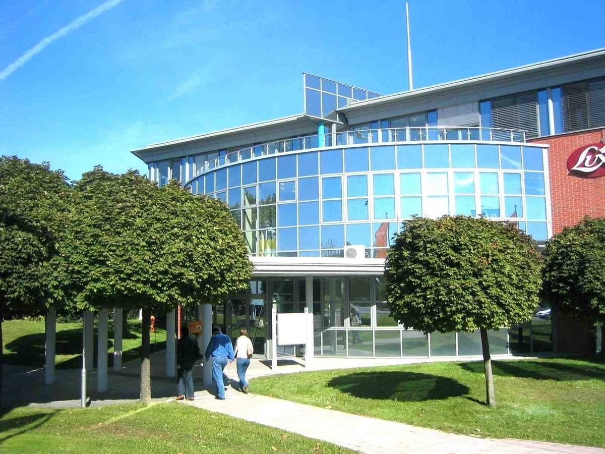 Modernes Bürogebäude mit geschwungener Glasfassade und gepflegten Grünflächen im Vordergrund.