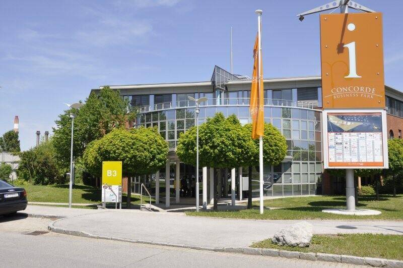 Eingangsbereich eines Geschäftsparks mit moderner Architektur, großen Fenstern und Hinweisschildern.