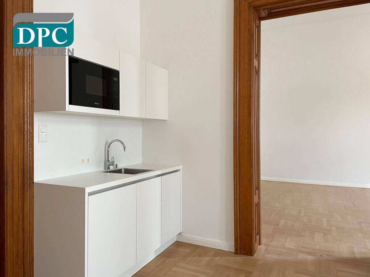 Moderne, kompakte Küchenzeile mit Spüle, Mikrowelle und weißen Schränken in einem hellen und funktionalen Design.