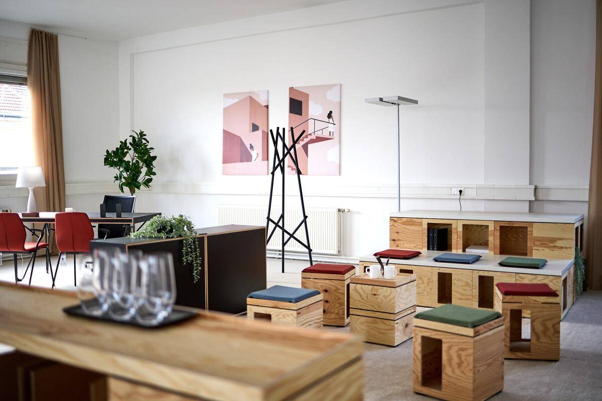 Kreativer Bürobereich mit Holzelementen, modernen Kunstwerken und flexiblen Sitzgelegenheiten für Zusammenarbeit.