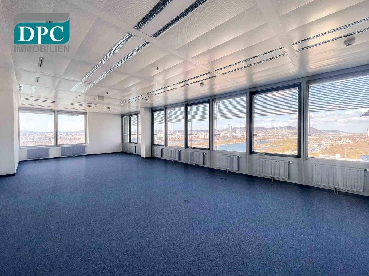 Helles Großraumbüro mit blauen Teppichfliesen und Panoramablick auf die Stadt, ideal für flexible Arbeitsbereiche.