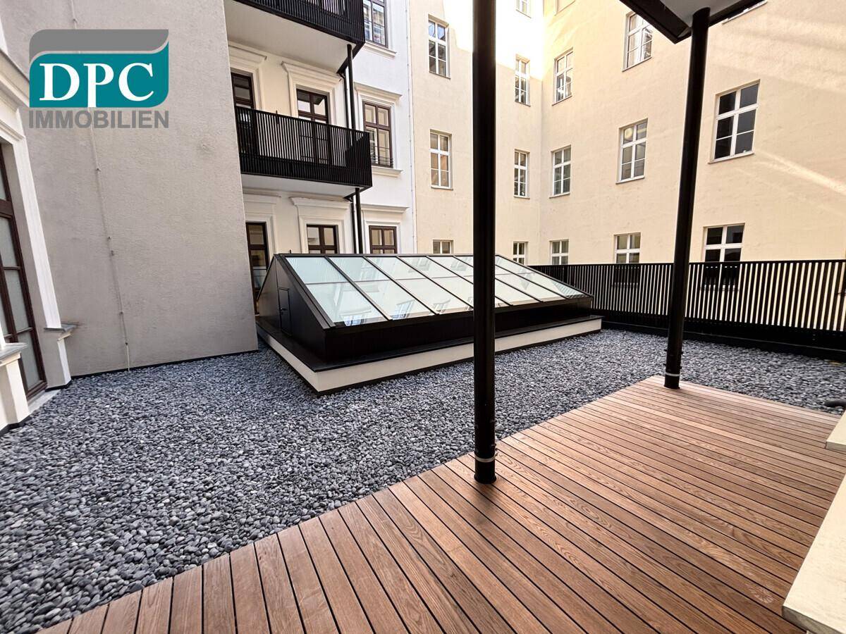 Attraktive Terrasse mit Holzboden und Kiesfläche, umgeben von einem Innenhofgebäude.