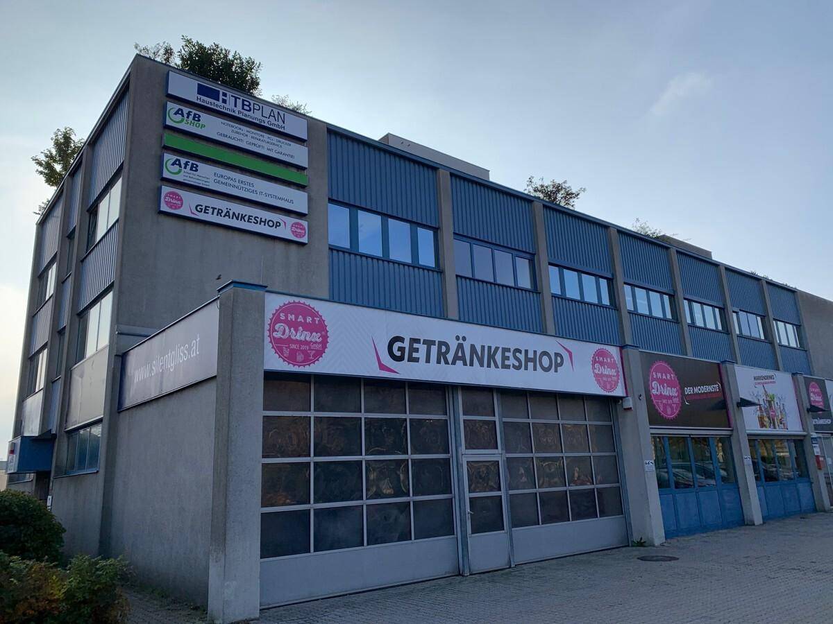 Seitenansicht eines Geschäftsgebäudes mit blauer Fassade, großen Fenstern und verschiedenen Firmenlogos.