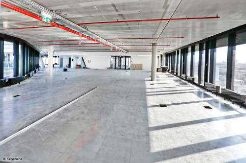 Weitläufiger, unmöblierter Bürobereich mit Betonboden und großen Fensterfronten, die viel Tageslicht hereinlassen.