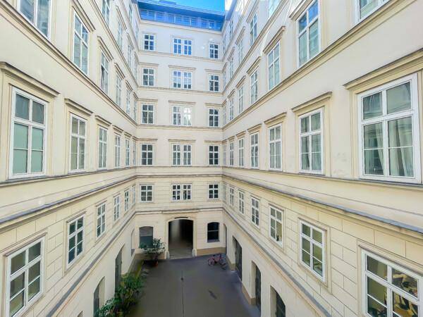 Blick von oben in einen hellen, quadratischen Innenhof mit vielen Fenstern und einem Fahrrad.