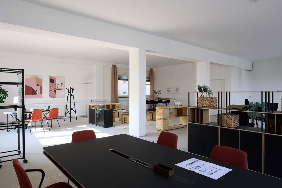 Geräumiger, offener Bürobereich mit verschiedenen Arbeitszonen, modernen Möbeln und minimalistischer Dekoration.