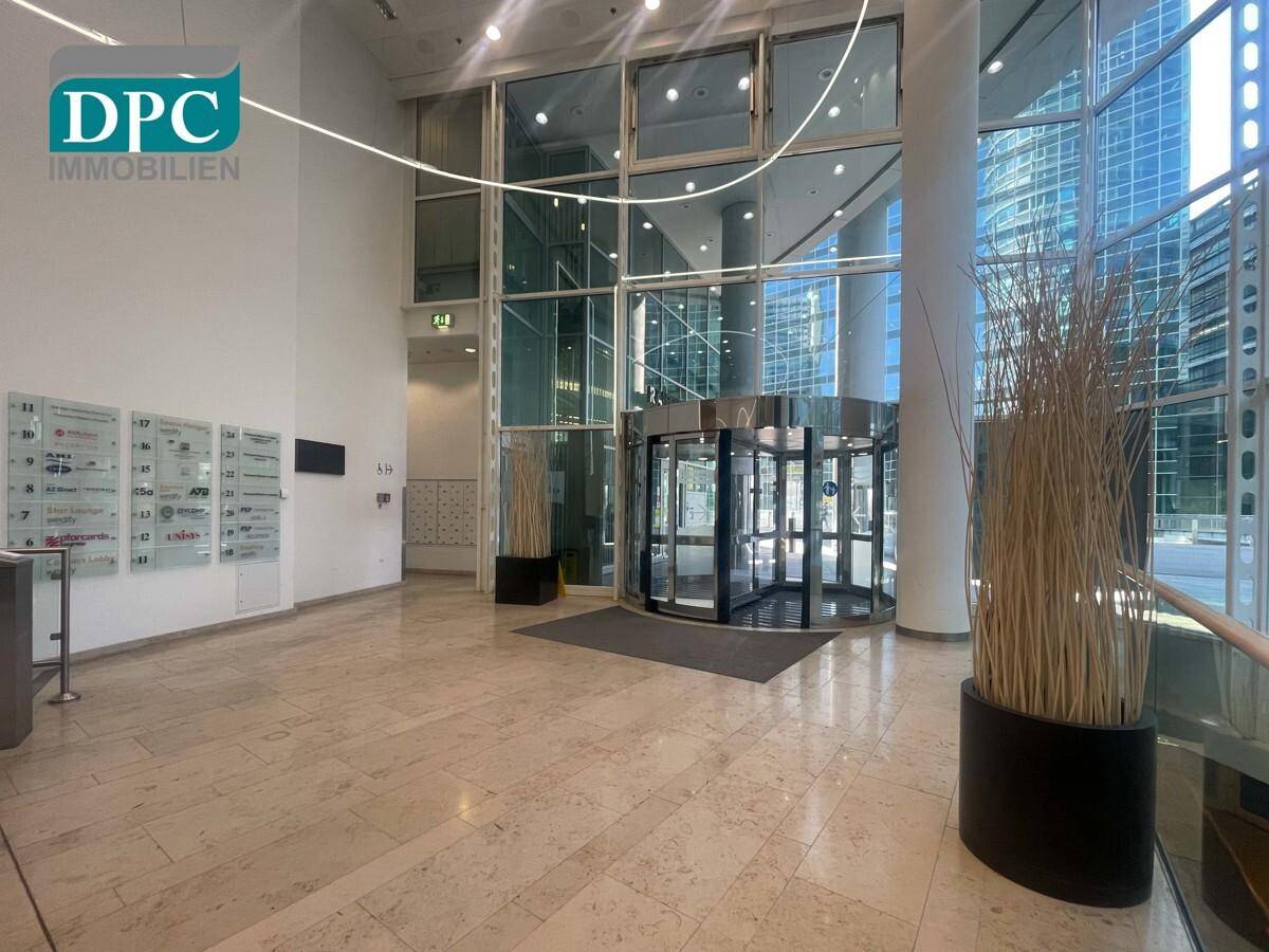 Helle und geräumige Lobby mit Marmorboden, Drehtür und Informationsanzeigen in einem modernen Gebäude.