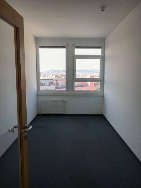 Kleiner, heller Büroraum mit zwei Fenstern, die einen Blick auf die Stadt bieten, und einem dunklen Teppichboden.