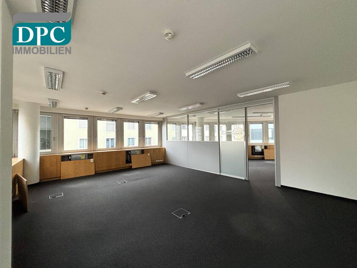 Modernes Büro mit Teppichboden, Glaswänden und einer langen Fensterfront mit Blick nach draußen.