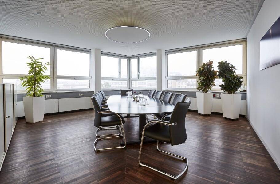 Geräumiger Konferenzraum mit großem Tisch, vielen Stühlen und weitem Ausblick durch die Fenster.