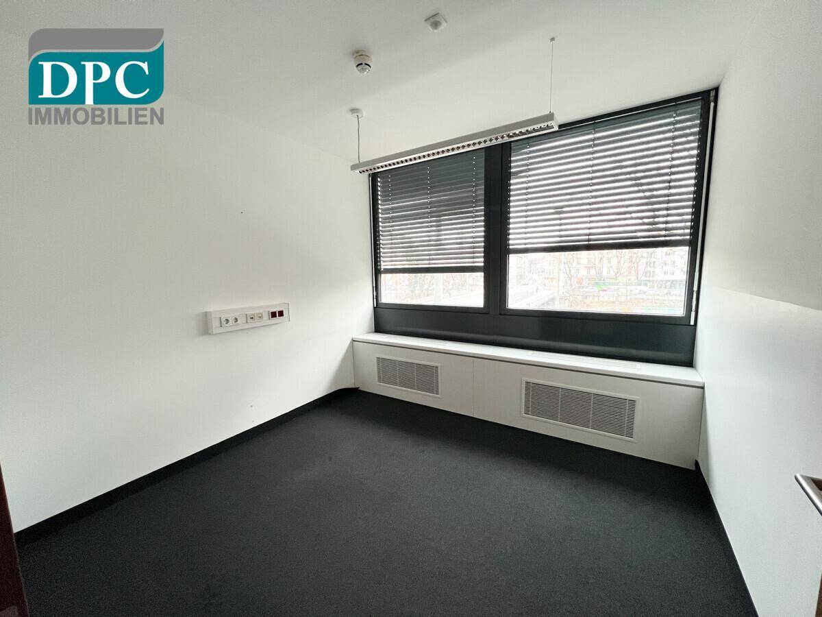 Büro mit großen Fenstern, Jalousien und schwarzem Teppichboden, ideal für konzentriertes Arbeiten.