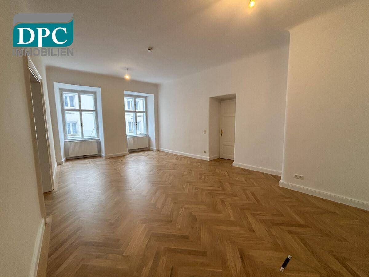 Geräumiges Wohnzimmer mit Fischgrätparkett, hohen Decken und großen Fenstern, bereit zur Einrichtung.