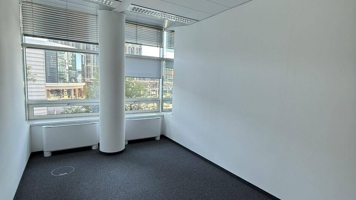 Eckbüro mit Teppichboden, weißer Säule und großen Fenstern, die viel Tageslicht hereinlassen.