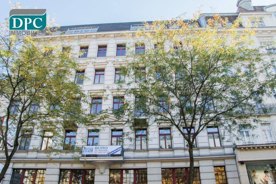 Gebäudefassade eines Mehrfamilienhauses mit Geschäften im Erdgeschoss und einem Bürovermietungsbanner an der Front.