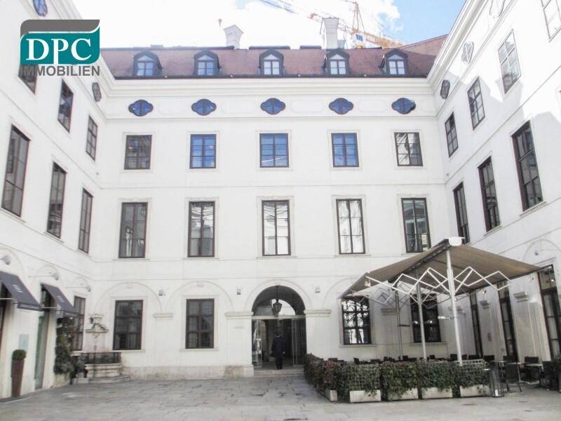 Ruhiger Innenhof mit historischer Architektur, Sitzgelegenheiten und einem Schirm für Schatten.
