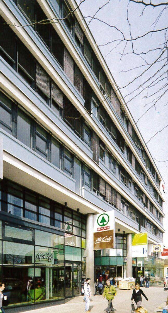 Modernes Geschäftsgebäude mit großen Glasfronten im Erdgeschoss und mehreren Etagen mit Fensterläden.