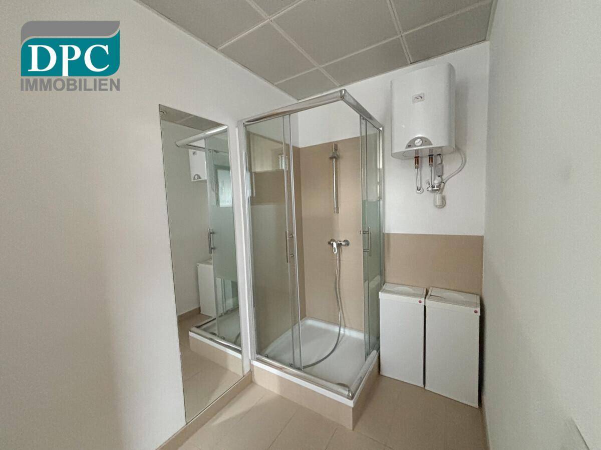 Badezimmer mit Eckduschkabine, Warmwasserboiler und hellen Fliesen, funktional und sauber.