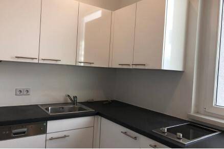 Moderne Küchenzeile mit weißen Hochglanzschränken, dunkler Arbeitsplatte und Induktionskochfeld.