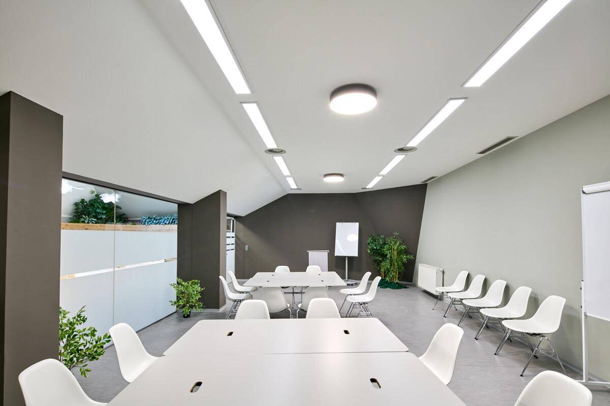 Moderner Konferenzraum mit weißen Tischen und Stühlen, effizienter Beleuchtung und schrägen Decken.
