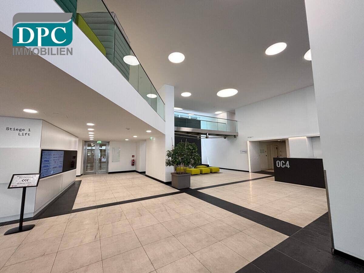 Moderne und helle Lobby mit hohen Decken, Fliesenboden und einem Empfangsbereich, inklusive Zugang zum Lift.