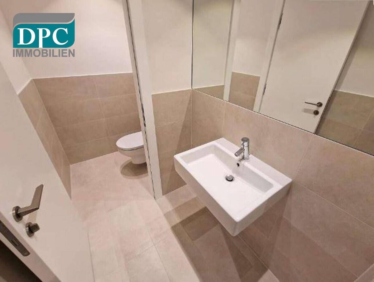 Modernes Gäste-WC mit wandhängendem Waschbecken und beigefarbenen Fliesen an Wänden und Boden.
